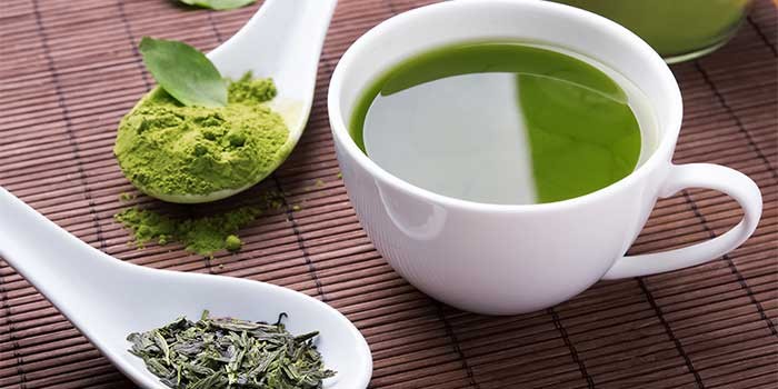 Taza de té verde junto a matcha y hojas